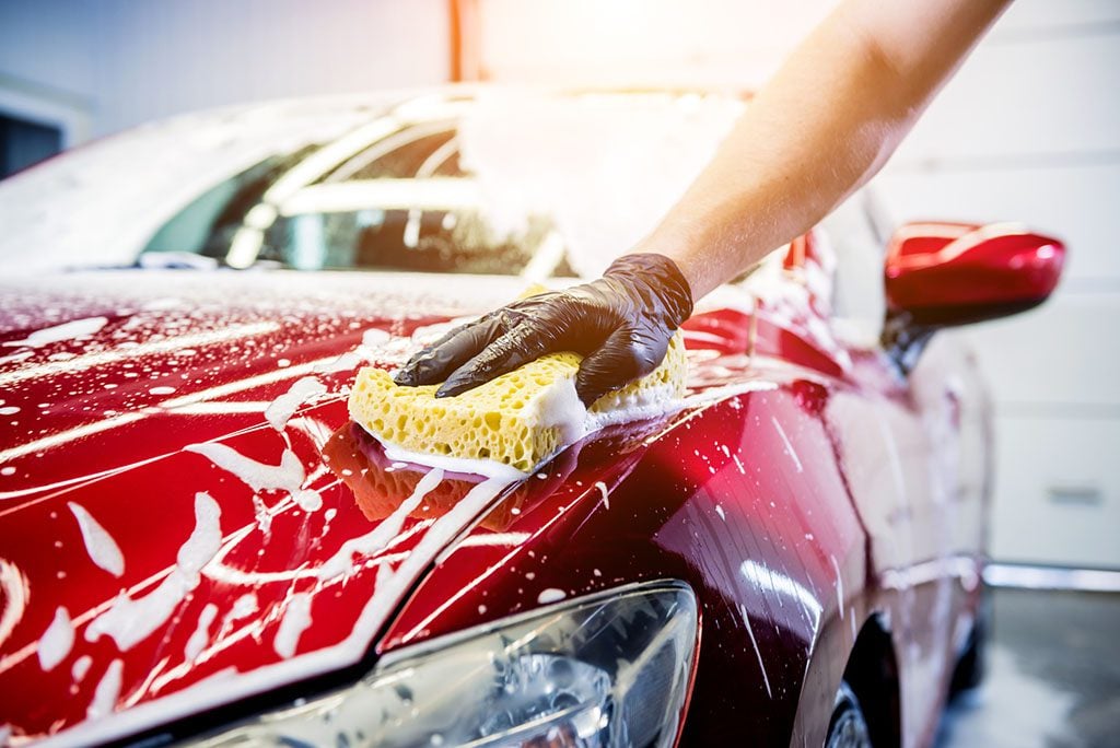 Worker washing red car with sponge on a Vinyl Wrapped Vehicle.