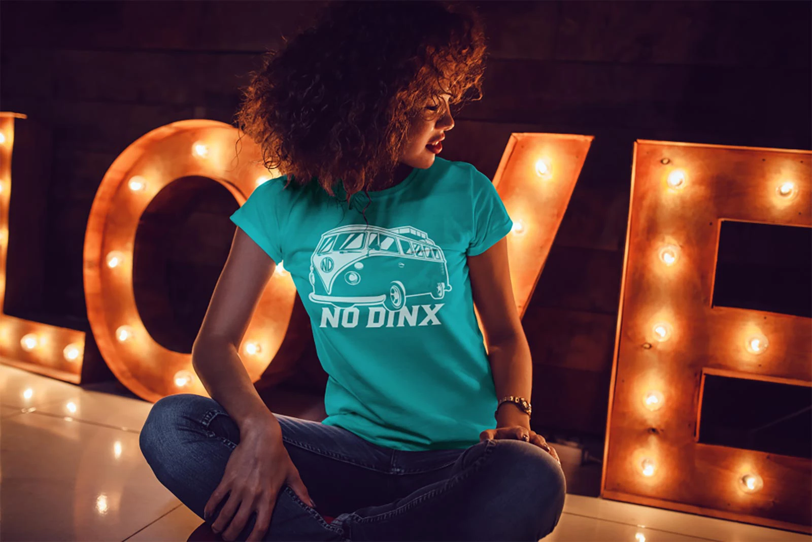Woman sitting cross legged in front of a sign wearing a No Dinx shirt