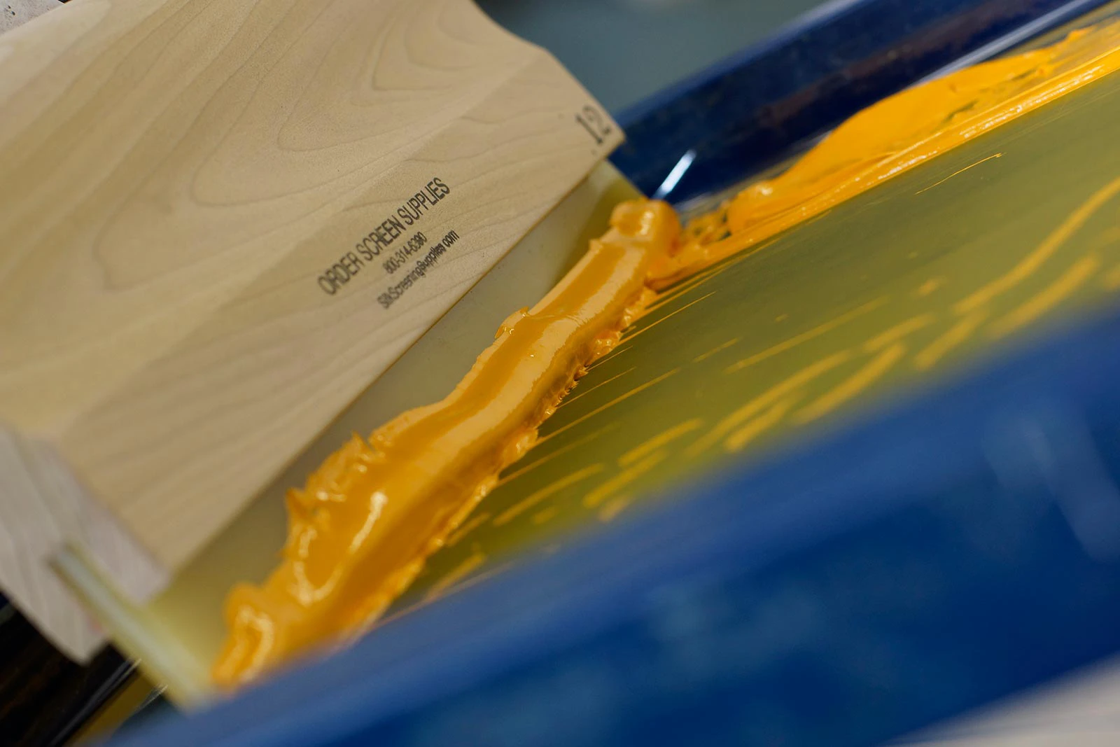 Screen printing squeegee pulling yellow ink across a screen